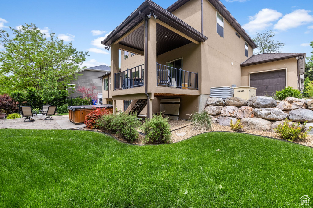 Rear view of property with a hot tub, stucco siding, a yard, and a patio area