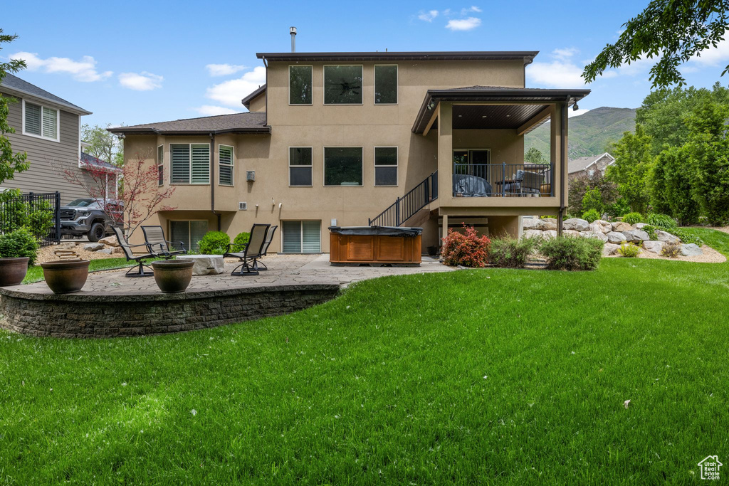 Back of property with a hot tub, stucco siding, a patio area, and a yard