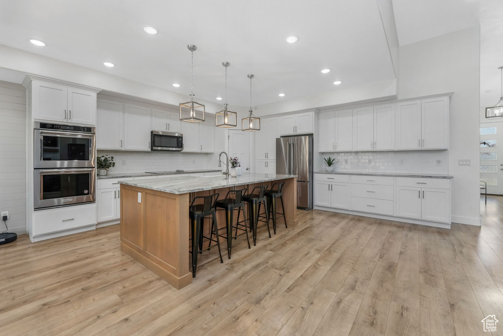 Kitchen featuring a breakfast bar area, white cabinets, stainless steel appliances, and light wood-style floors