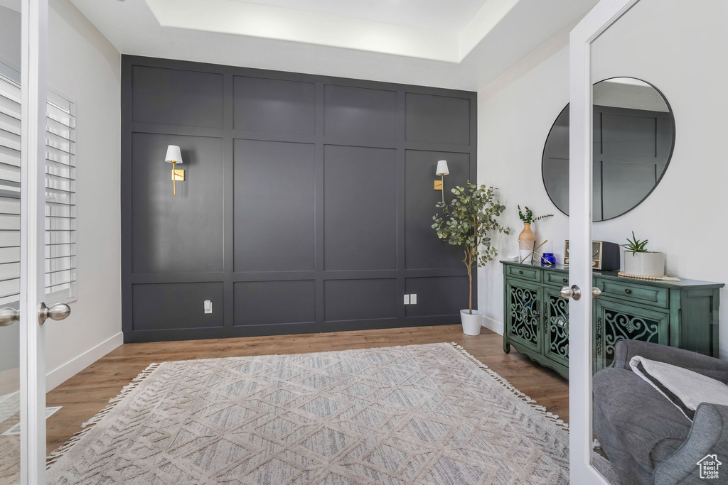 Interior space with a tray ceiling, a decorative wall, french doors, and light wood-type flooring