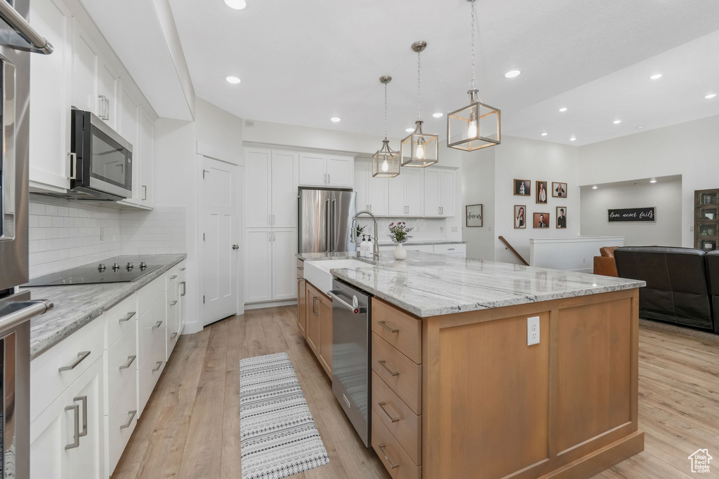 Kitchen featuring light wood-type flooring, backsplash, appliances with stainless steel finishes, and white cabinetry