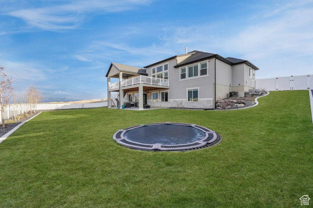 Rear view of house with a yard, a fenced backyard, stucco siding, and a trampoline