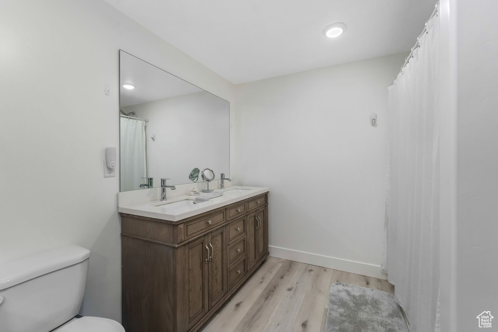 Full bathroom featuring baseboards, toilet, double vanity, wood finished floors, and a sink