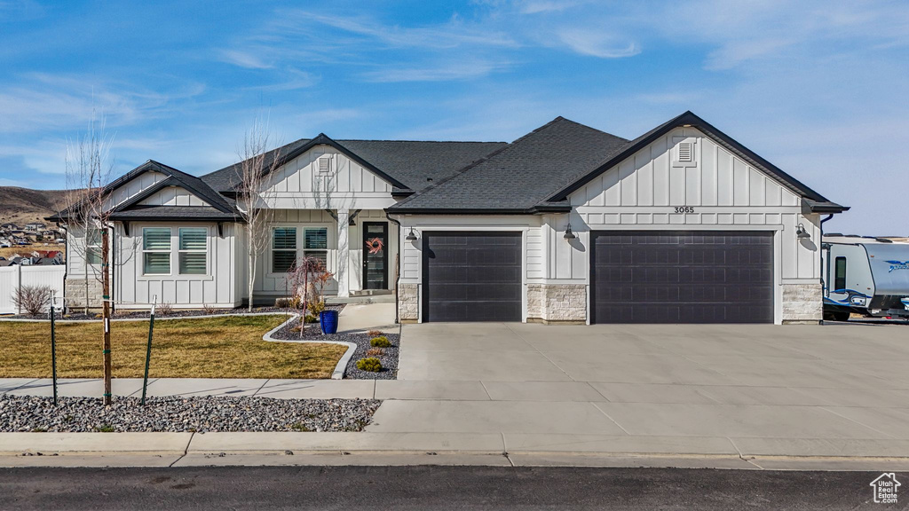 Modern farmhouse with board and batten siding, a shingled roof, a front yard, a garage, and driveway