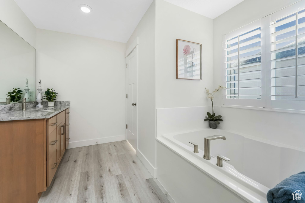 Bathroom with vanity, wood finished floors, baseboards, recessed lighting, and a bath