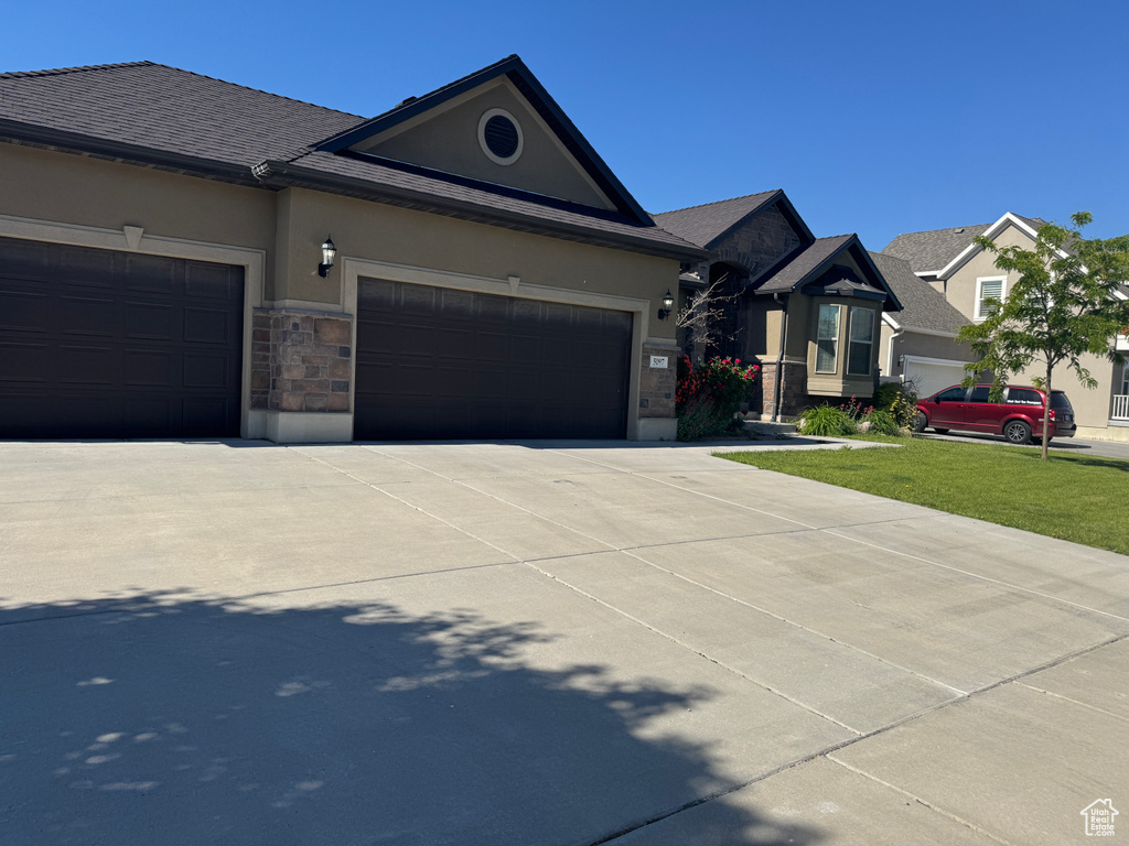 Single story home featuring stucco siding, a garage, concrete driveway, stone siding, and a front yard