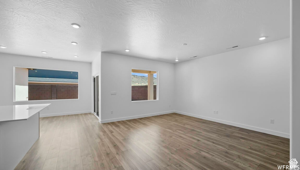 Unfurnished living room with recessed lighting, wood finished floors, baseboards, and a textured ceiling