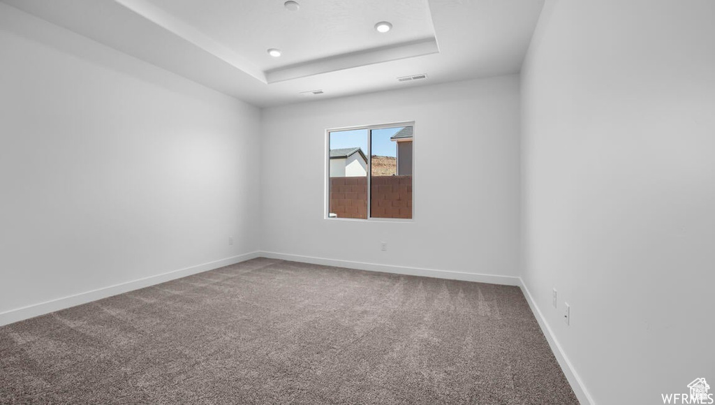 Carpeted empty room featuring a raised ceiling, visible vents, and baseboards