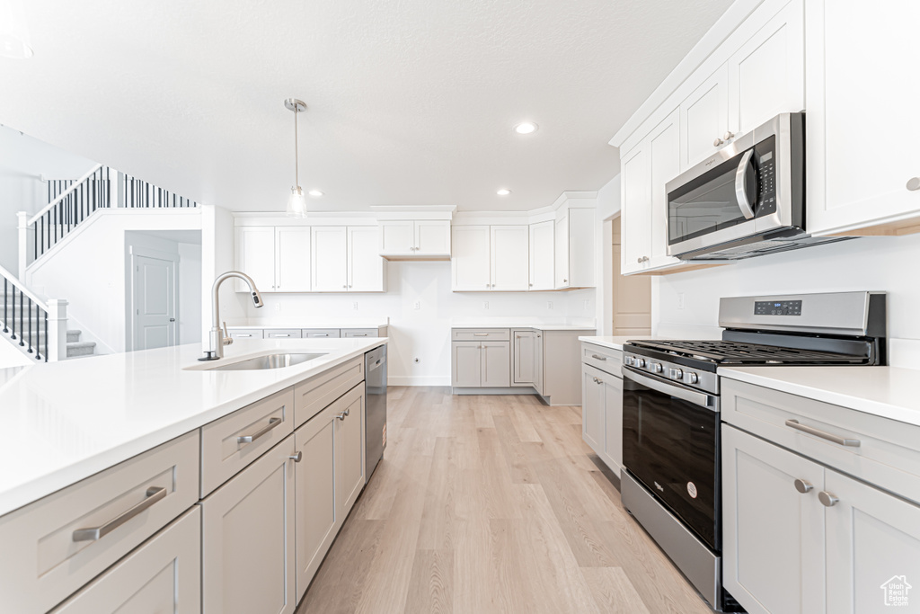 Kitchen with appliances with stainless steel finishes, a sink, light wood-type flooring, recessed lighting, and decorative light fixtures
