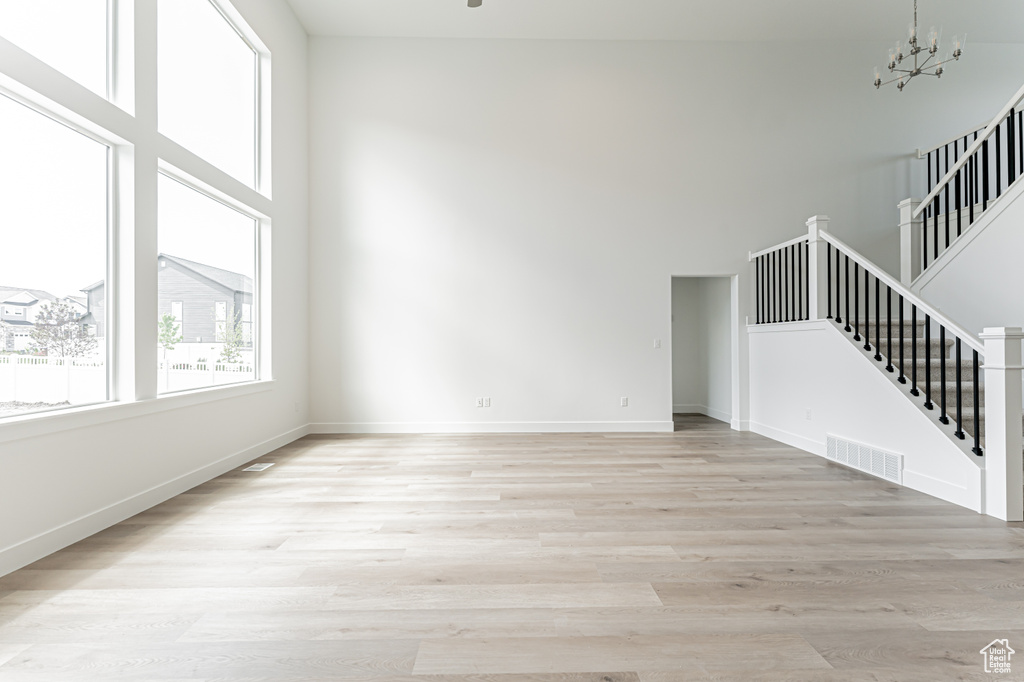 Unfurnished living room with stairway, light wood-style floors, a high ceiling, and baseboards