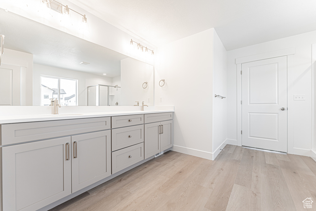 Full bathroom with double vanity, wood finished floors, a shower stall, and baseboards