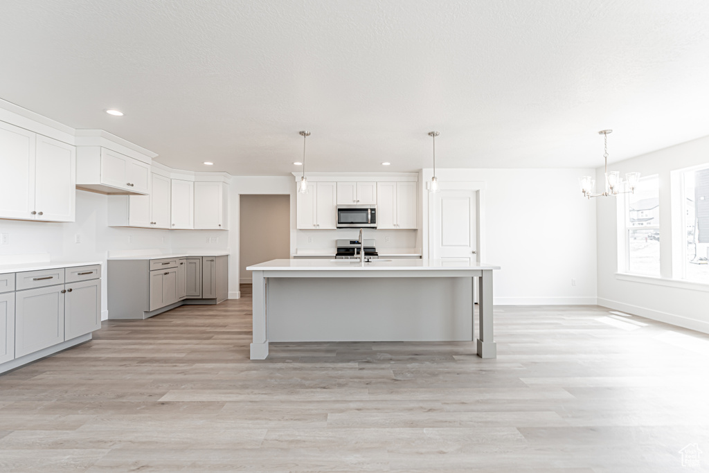 Kitchen with stainless steel microwave, a chandelier, recessed lighting, light wood finished floors, and baseboards