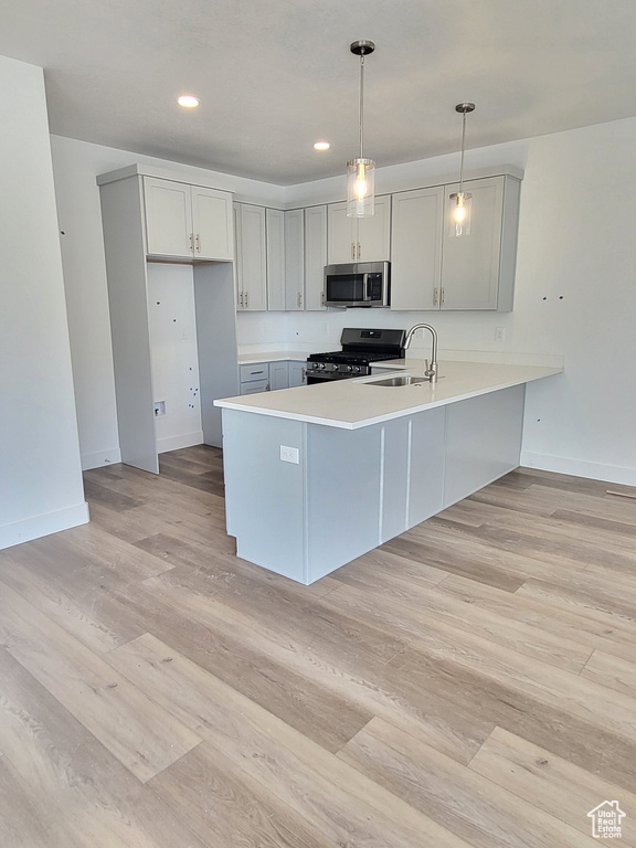 Kitchen featuring baseboards, a sink, appliances with stainless steel finishes, a peninsula, and light wood finished floors