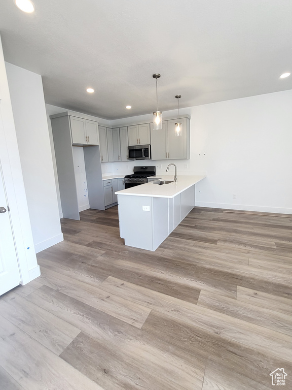 Kitchen featuring stainless steel microwave, range with gas stovetop, a peninsula, gray cabinetry, and a sink