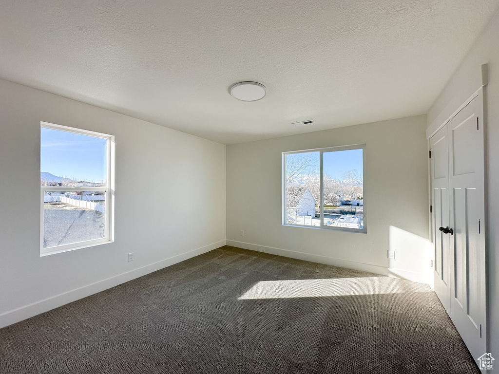 Unfurnished bedroom featuring dark carpet, a textured ceiling, and baseboards