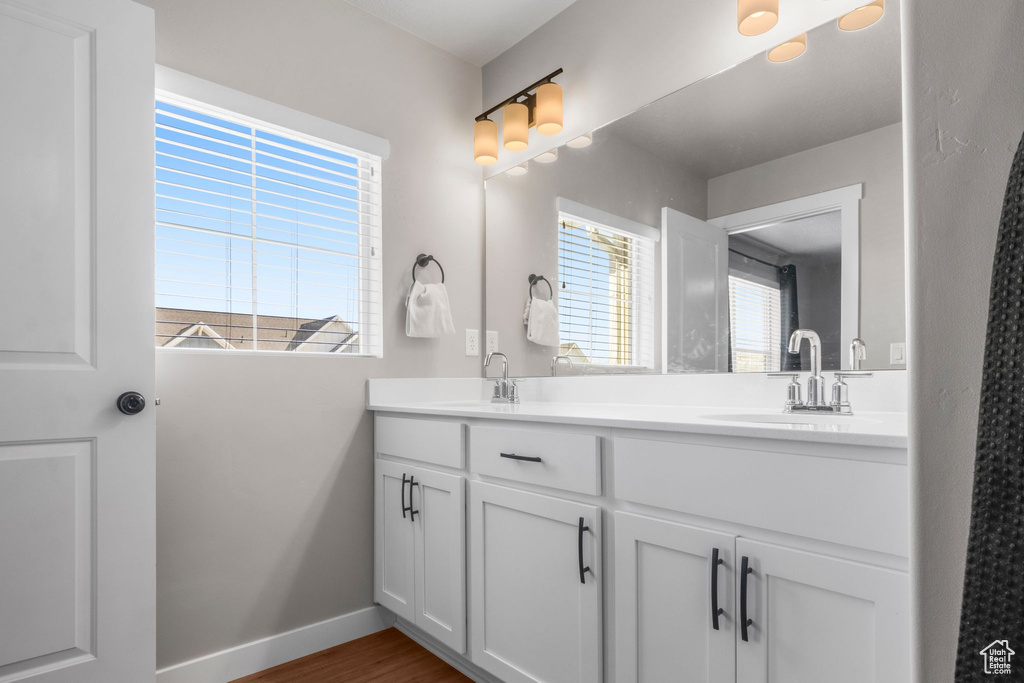 Full bathroom featuring double vanity, wood finished floors, baseboards, and a sink