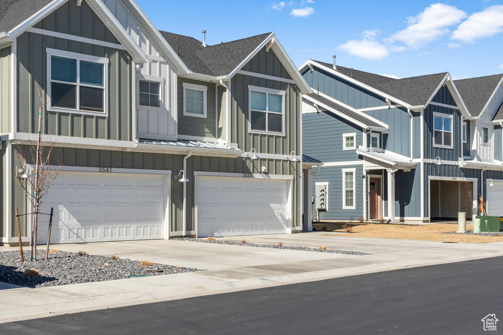 View of property featuring an attached garage, roof with shingles, board and batten siding, and driveway