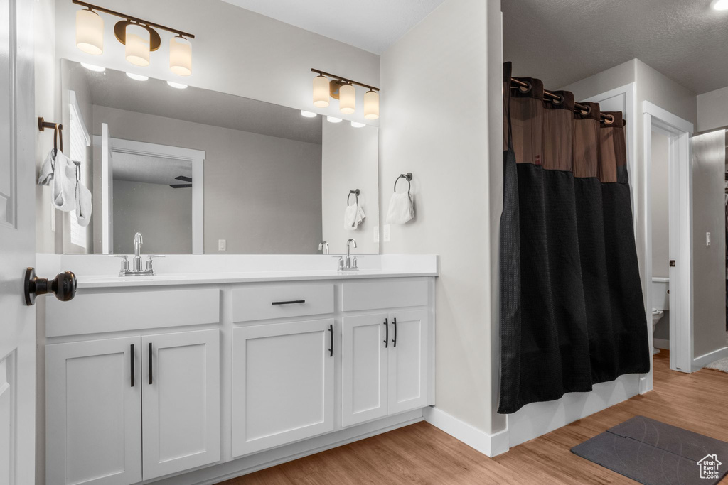 Bathroom with a shower with shower curtain, wood finished floors, baseboards, double vanity, and a sink
