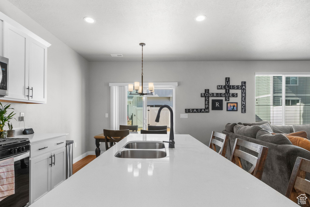 Kitchen with a chandelier, pendant lighting, light countertops, gas range oven, and a sink