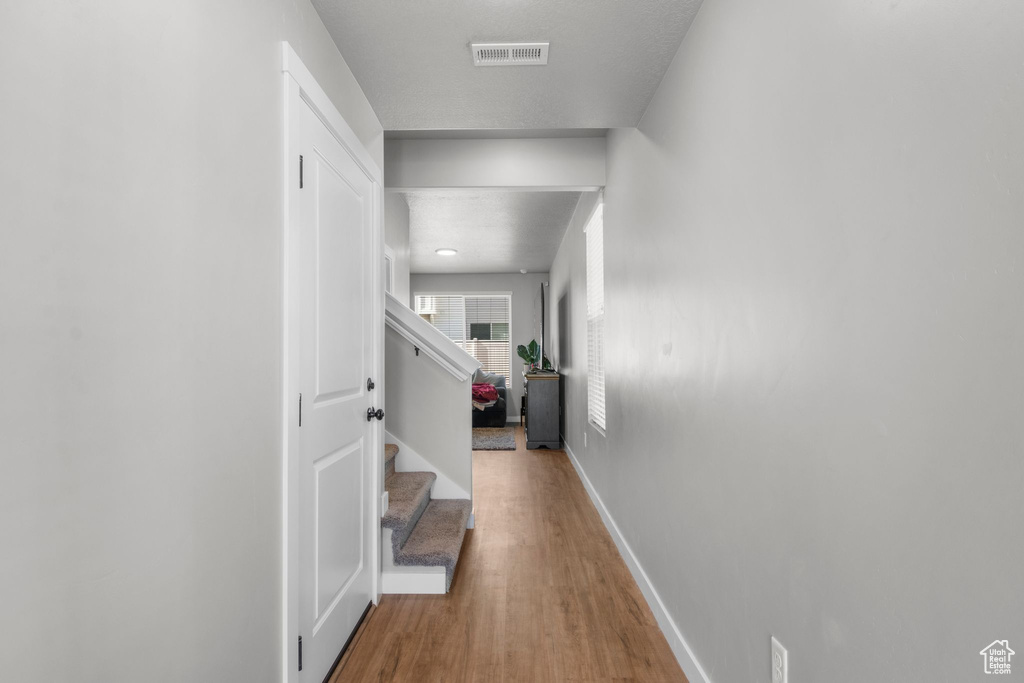 Hall with stairs, wood finished floors, baseboards, and visible vents
