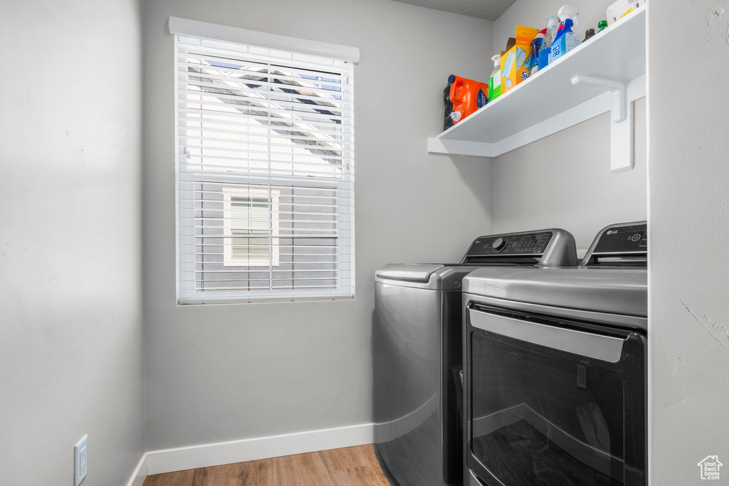 Clothes washing area with washer and clothes dryer, laundry area, baseboards, and wood finished floors