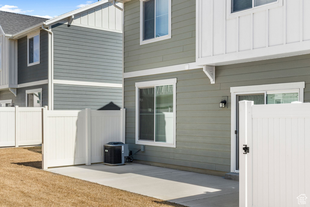 Entrance to property featuring central air condition unit, fence, board and batten siding, roof with shingles, and a patio area