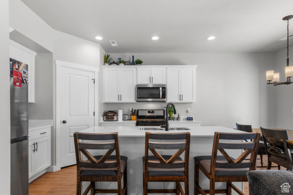 Kitchen with light wood-style flooring, a sink, stainless steel appliances, light countertops, and a kitchen breakfast bar