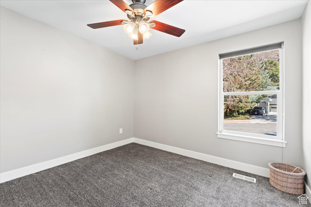 Spare room with visible vents, a ceiling fan, baseboards, and dark colored carpet