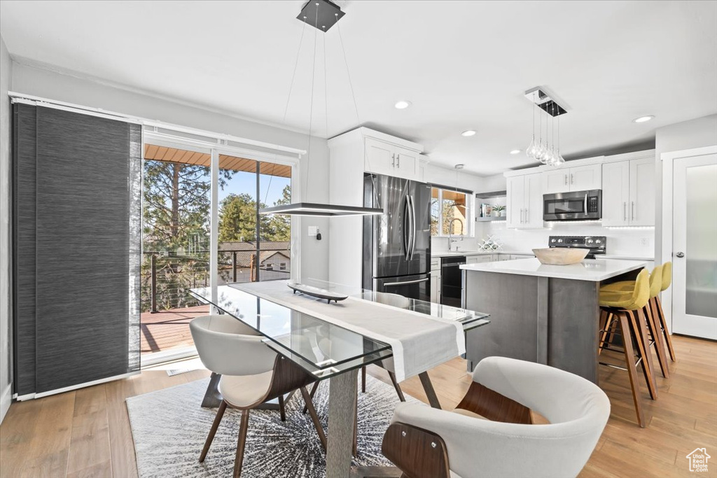 Kitchen featuring a center island, stainless steel appliances, light wood-style floors, white cabinets, and light countertops