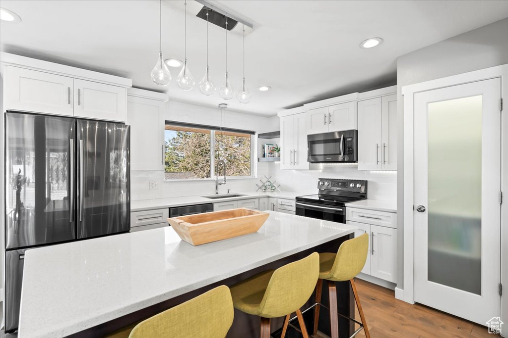 Kitchen with tasteful backsplash, appliances with stainless steel finishes, a kitchen breakfast bar, white cabinets, and a sink