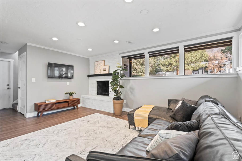 Living area featuring a brick fireplace, recessed lighting, wood finished floors, and ornamental molding