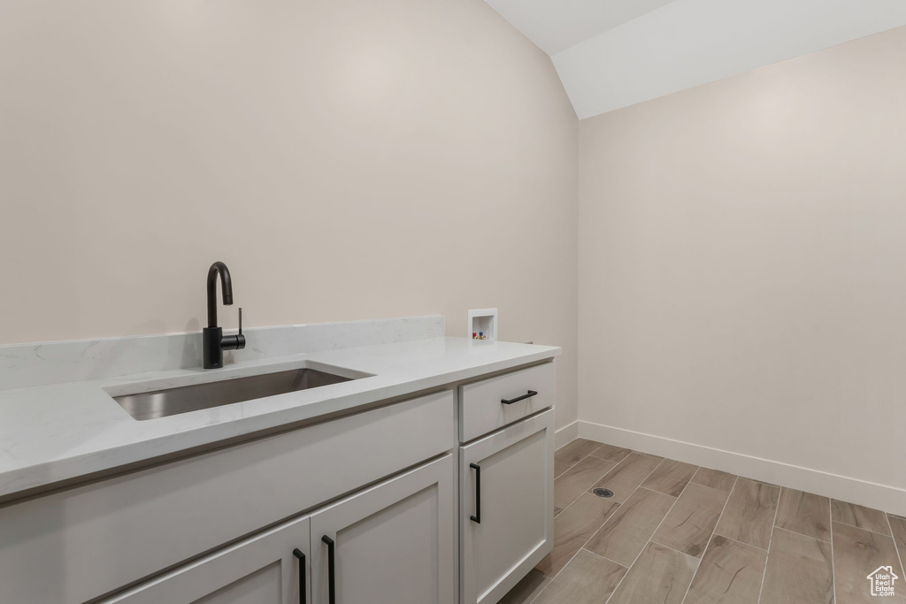 Clothes washing area with baseboards, wood tiled floor, washer hookup, cabinet space, and a sink