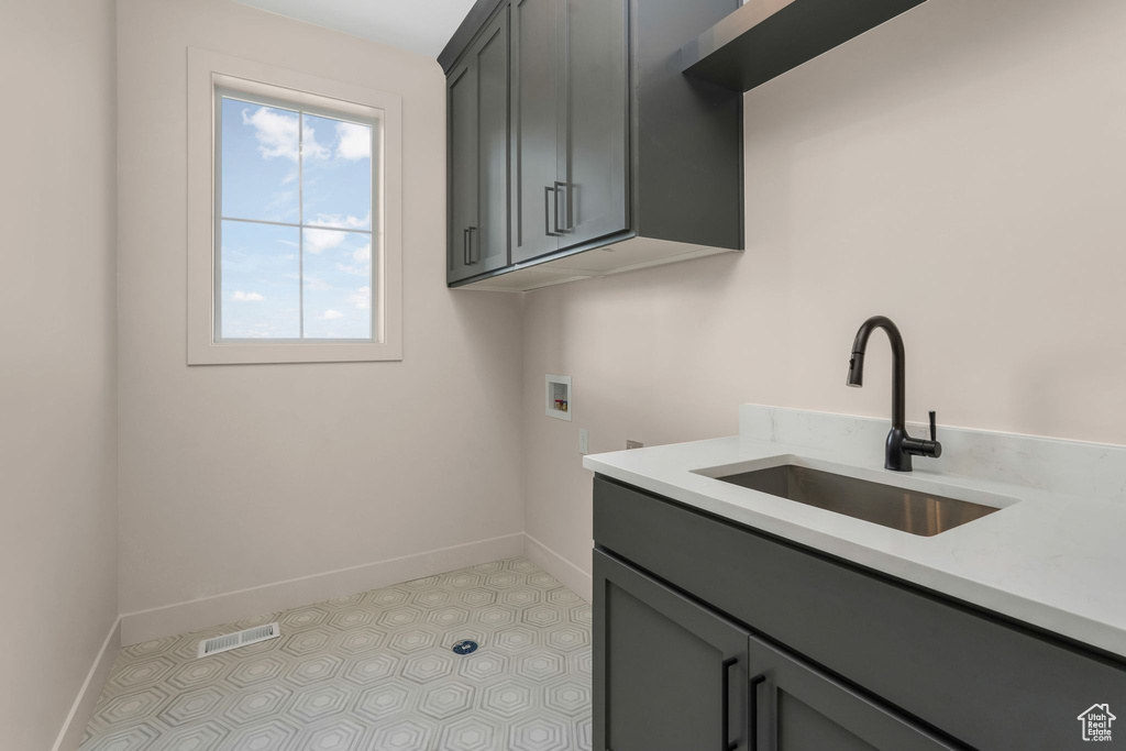 Clothes washing area featuring visible vents, baseboards, washer hookup, cabinet space, and a sink