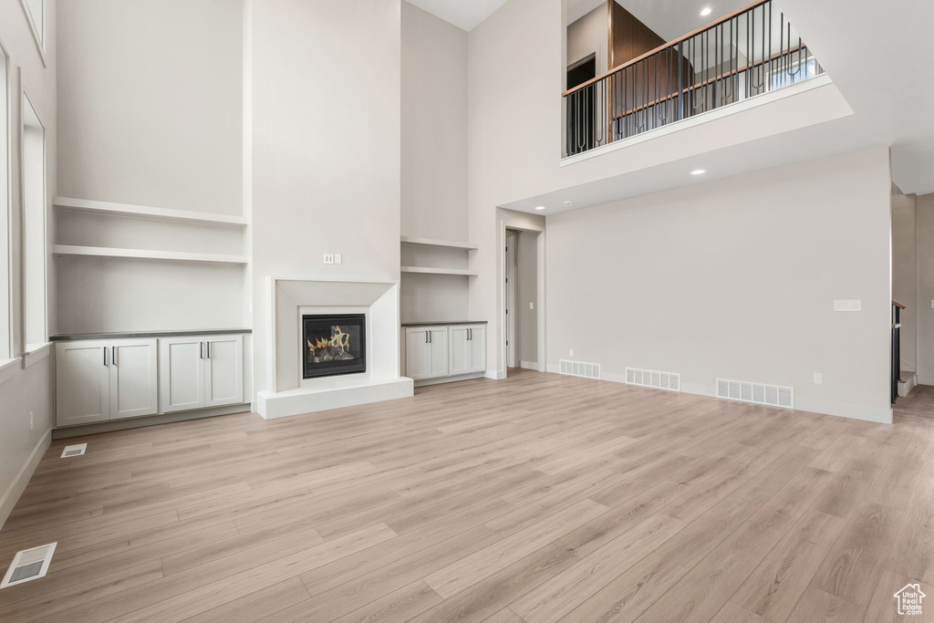 Unfurnished living room with visible vents, a glass covered fireplace, and light wood-style flooring