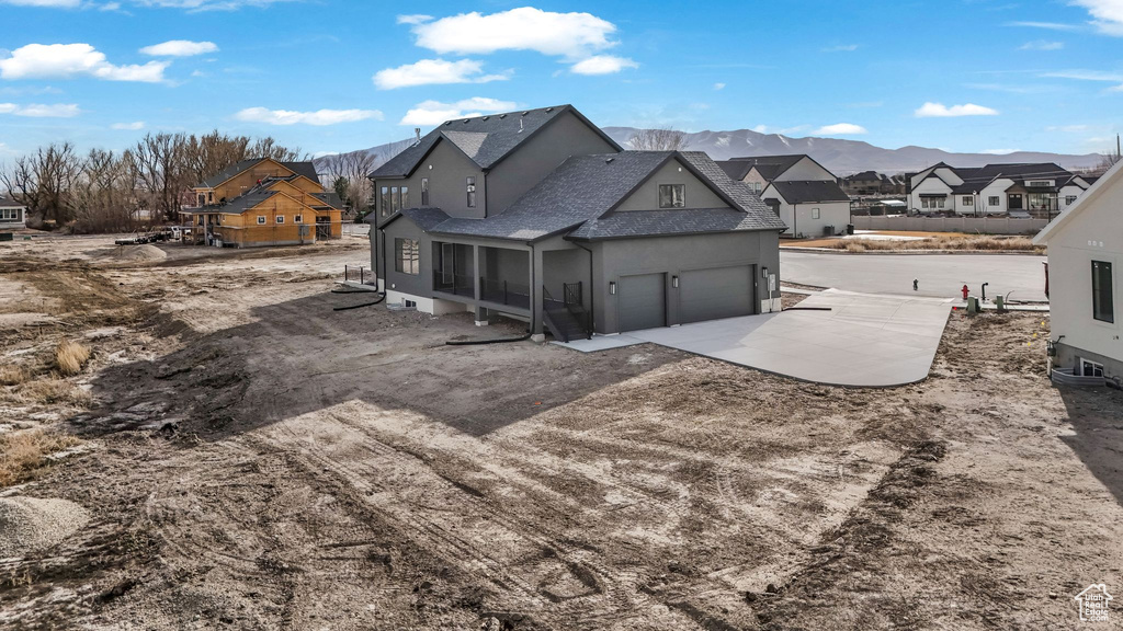 Back of property with an attached garage, a shingled roof, stucco siding, concrete driveway, and a residential view