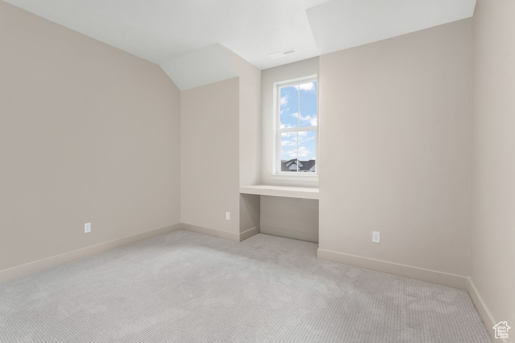 Empty room featuring lofted ceiling, light colored carpet, baseboards, and visible vents