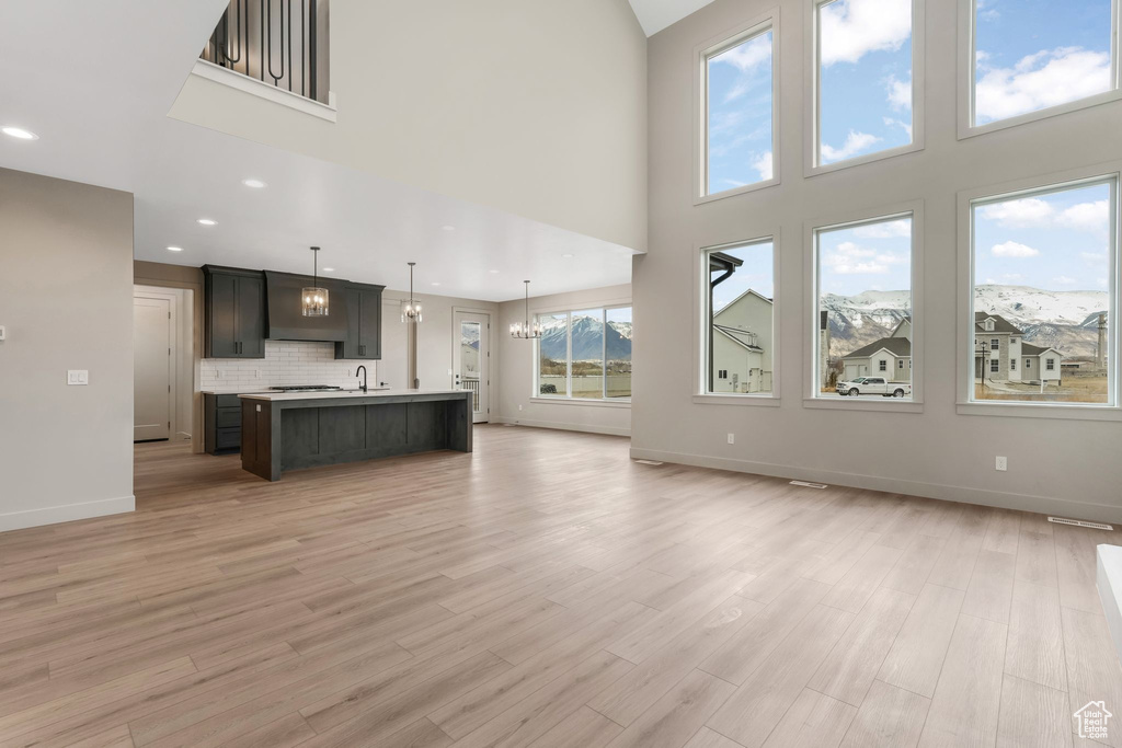 Unfurnished living room with recessed lighting, a notable chandelier, baseboards, and light wood-style floors