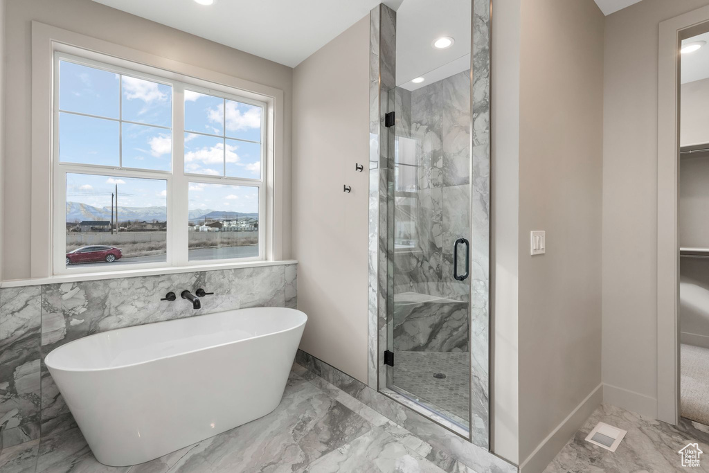 Bathroom featuring a freestanding tub, a walk in closet, marble finish floor, a stall shower, and recessed lighting