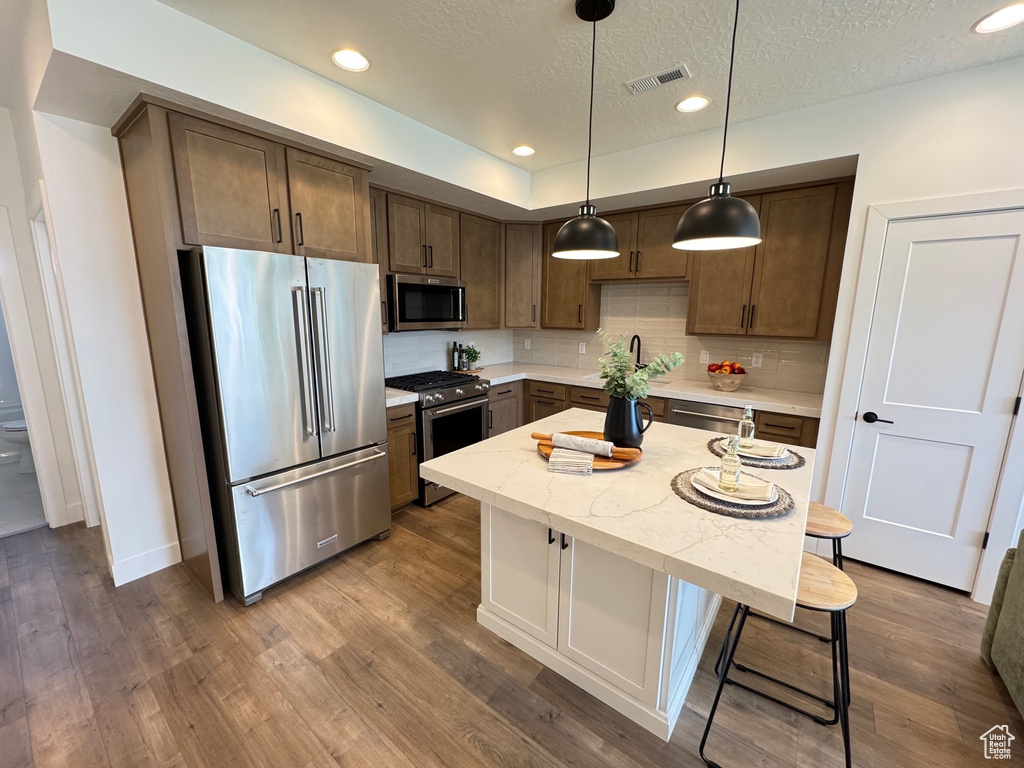 Kitchen with appliances with stainless steel finishes, a breakfast bar area, a sink, decorative backsplash, and dark wood-style flooring