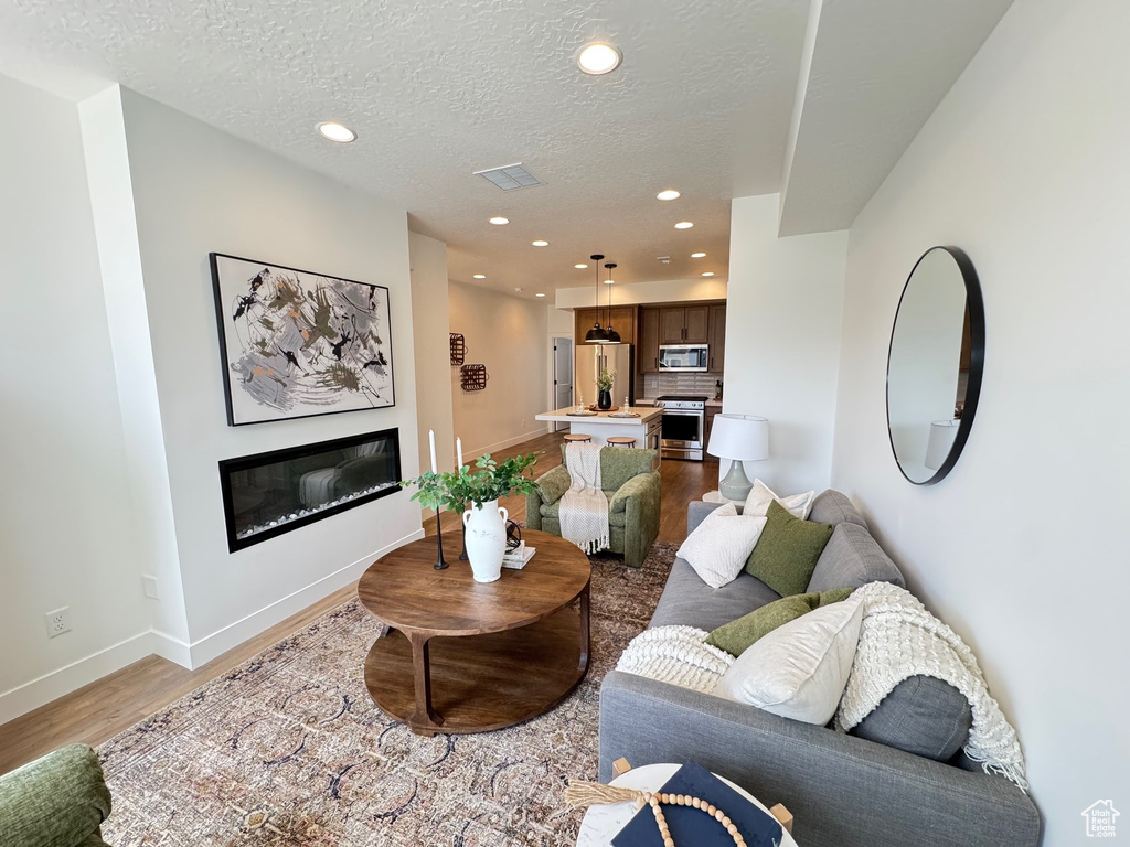 Living room with a glass covered fireplace, light wood finished floors, baseboards, recessed lighting, and a textured ceiling