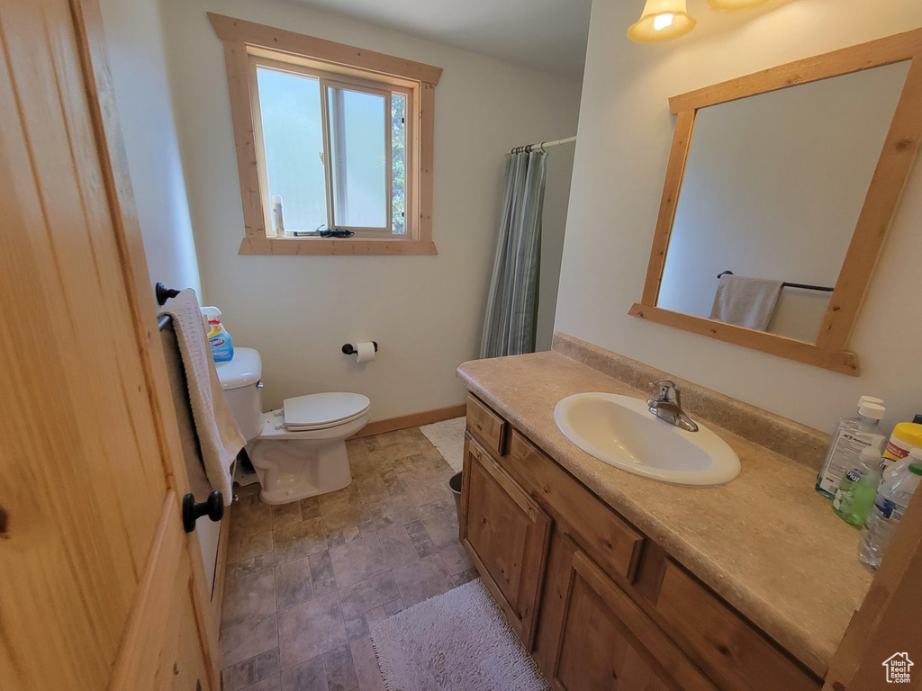 Full bathroom with vanity, a shower with shower curtain, baseboards, stone finish flooring, and toilet