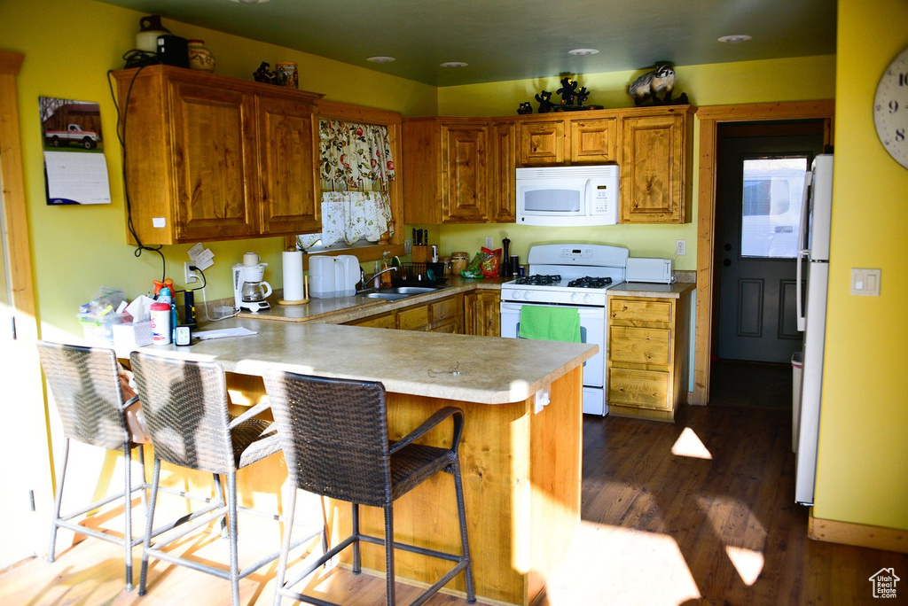 Kitchen featuring white appliances, a peninsula, brown cabinets, and a sink