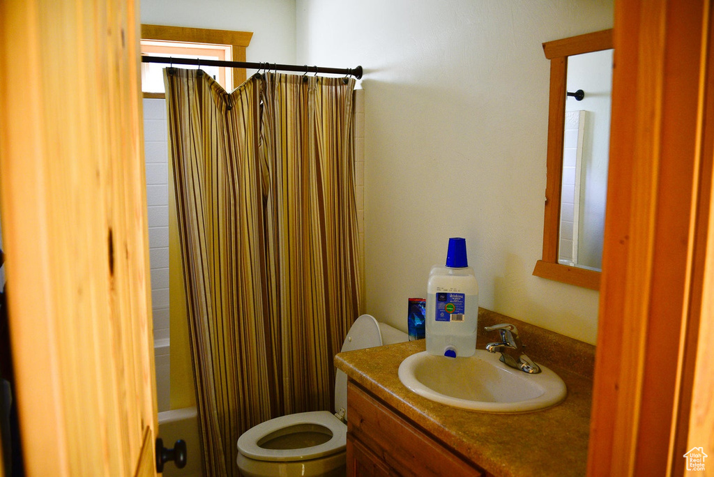 Bathroom featuring shower / bath combination with curtain, toilet, and vanity