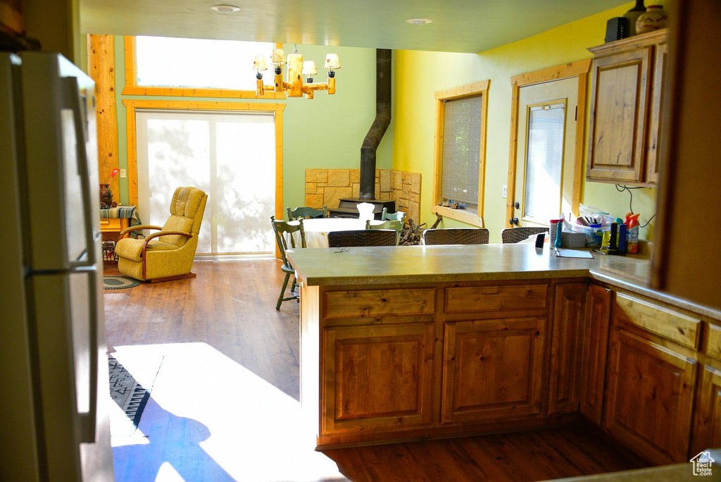 Kitchen featuring a notable chandelier, dark wood finished floors, freestanding refrigerator, a peninsula, and a wood stove