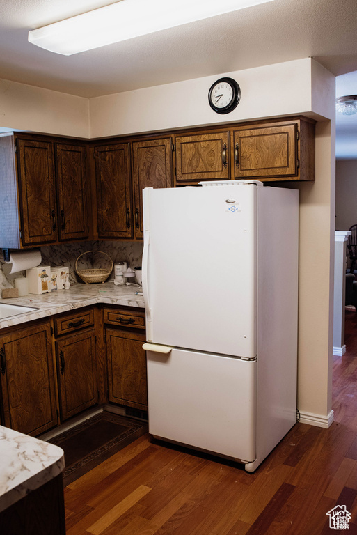 Kitchen with baseboards, light countertops, decorative backsplash, freestanding refrigerator, and dark wood-style flooring