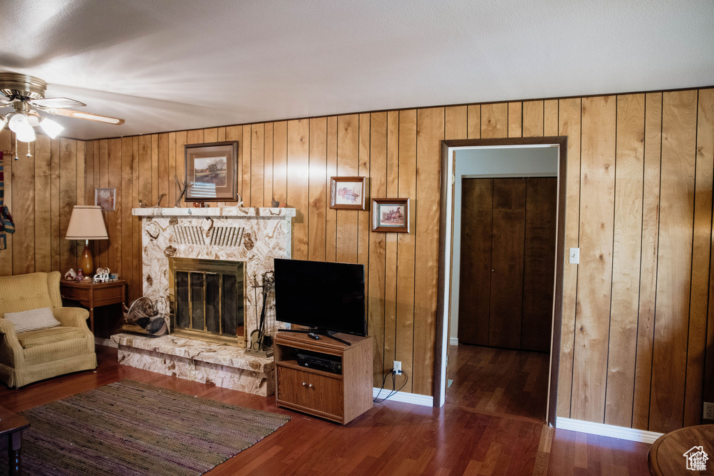 Living room with ceiling fan, wooden walls, a stone fireplace, and wood finished floors
