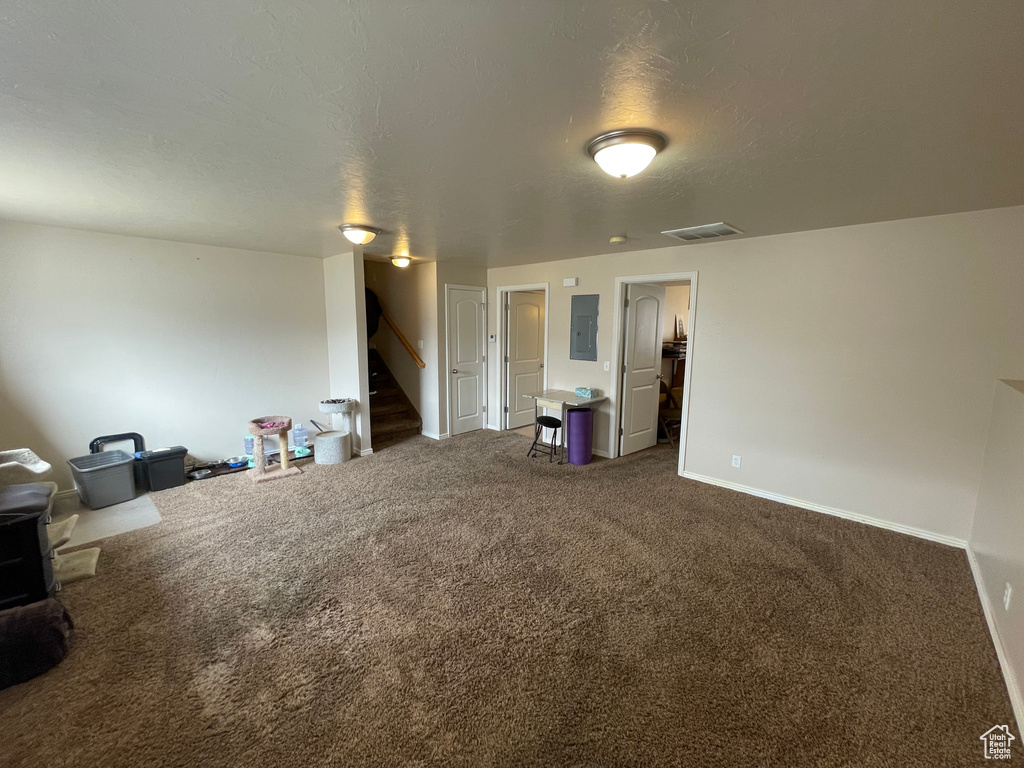 Unfurnished living room with visible vents, stairs, electric panel, a textured ceiling, and dark colored carpet