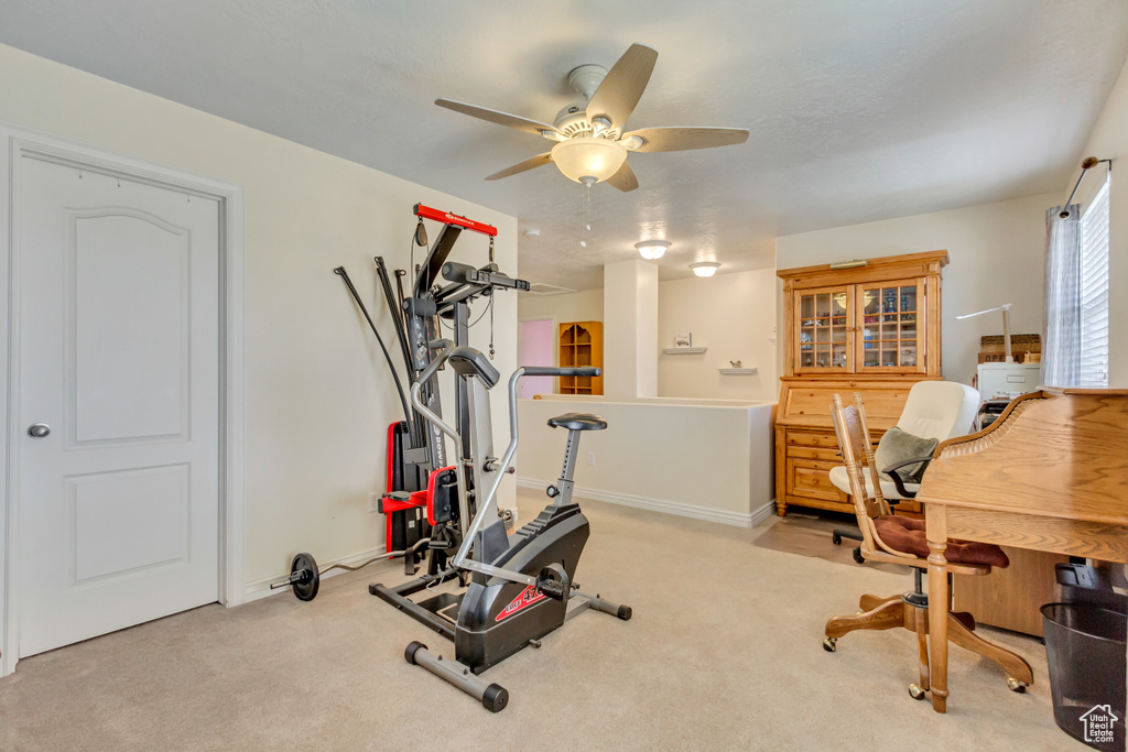 Exercise area featuring light colored carpet, a ceiling fan, and baseboards
