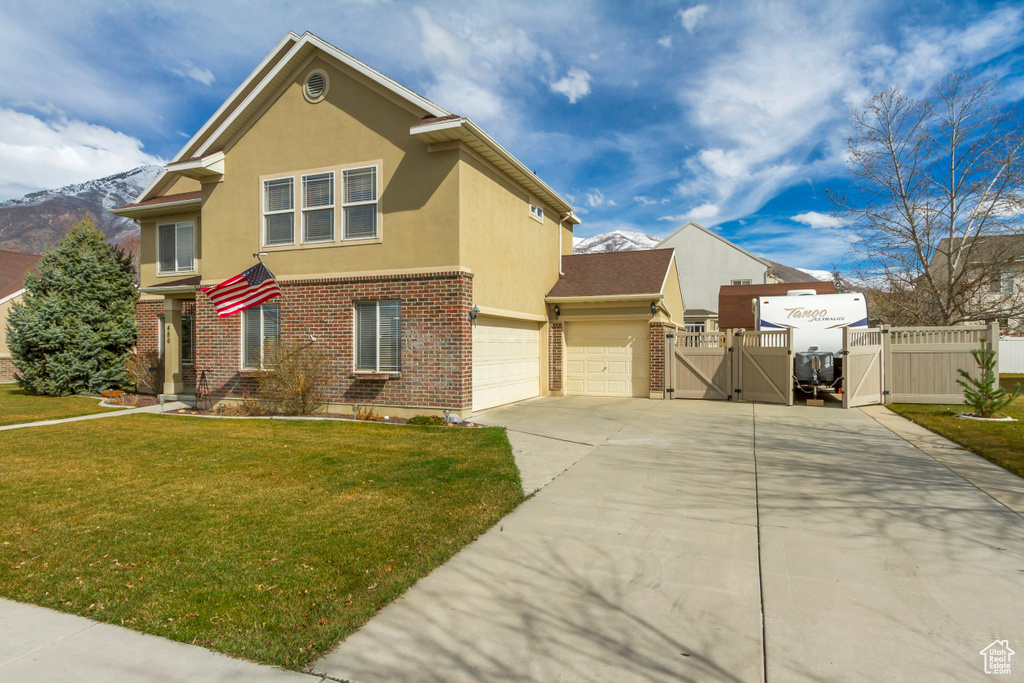 Traditional home featuring a front yard, a gate, driveway, stucco siding, and brick siding