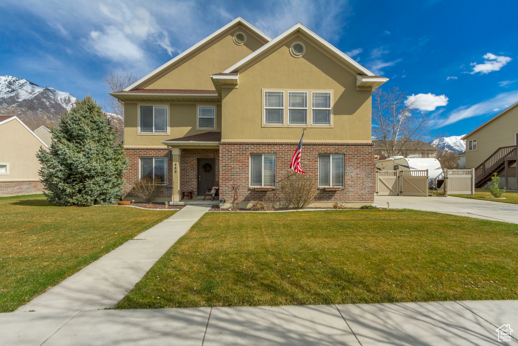Traditional home with a gate, brick siding, stucco siding, a front lawn, and a mountain view